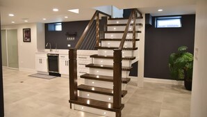 Eine moderne Küche mit eingebautem Geschirrspüler, weißen Schränken und einer Holztreppe mit Beleuchtung.