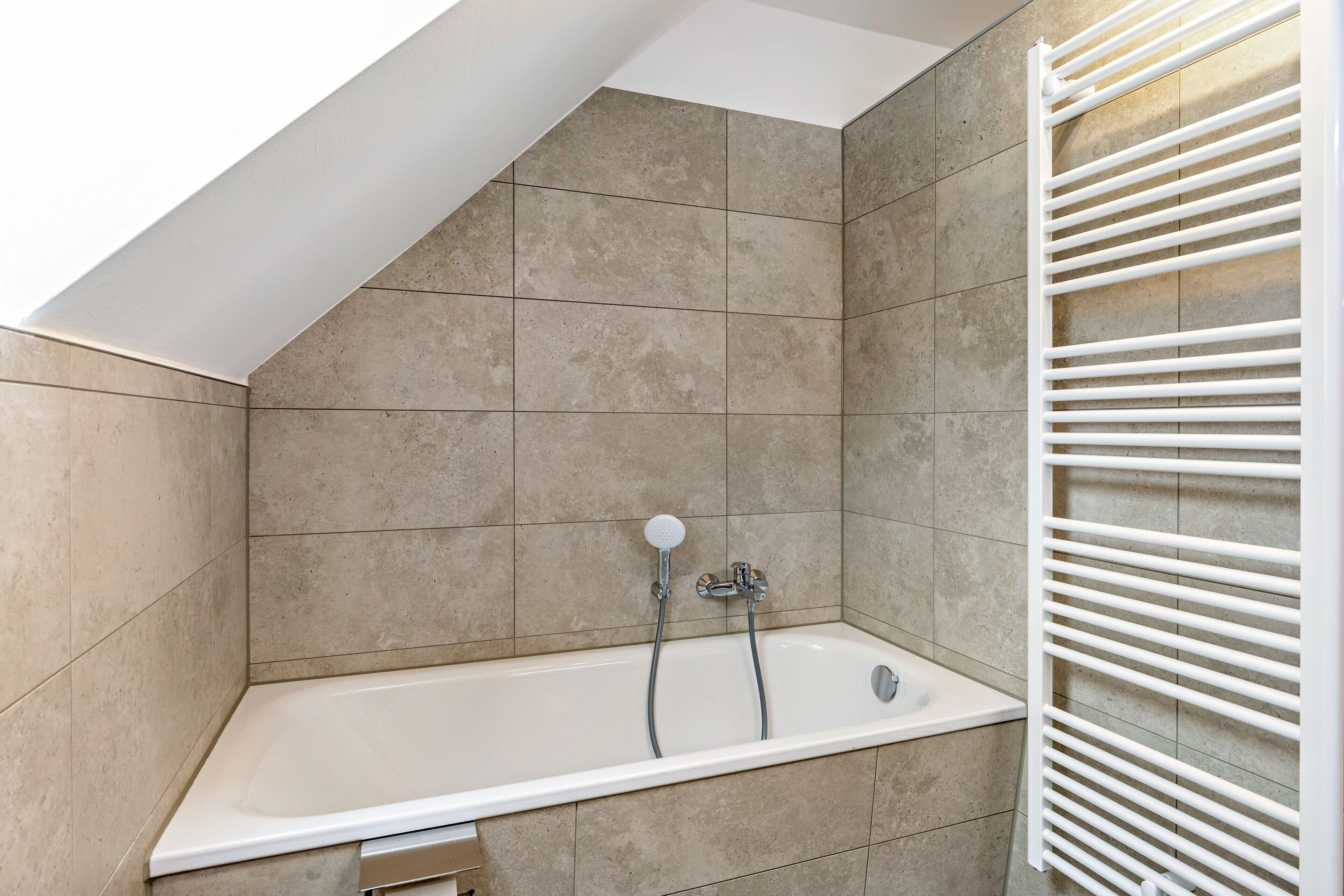 Une salle de bain avec une baignoire, une douche et un radiateur blanc.