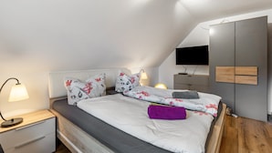 Une chambre à coucher avec un lit, des tables de chevet, une lampe, une télévision et une armoire.