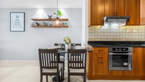 Una cocina moderna con armarios de madera, horno empotrado y comedor con dos sillas y una mesa para dos.