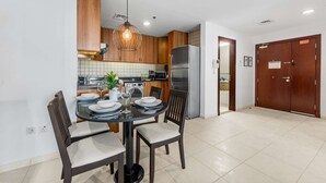 Una cocina moderna con armarios de madera, un refrigerador de acero inoxidable y un comedor con mesa y sillas de vidrio.