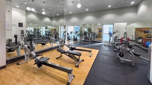 Un gimnasio con paredes de espejo, diverso equipo de ejercicio y suelo de madera.