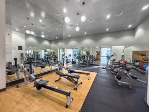 Ein Fitnessraum mit Spiegelwänden, unterschiedlicher Trainingsausstattung und Holzboden.