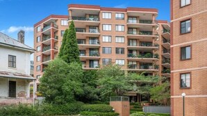 A multi-story residential building with balconies, a well-maintained lawn, and a tall tree in the foreground. - Stunning Downtown Retreat With City Views (Surry Hills)