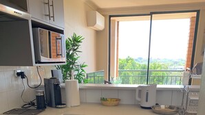 A compact kitchen with grey cabinets, a built-in oven, a coffee maker, and a window with a view of greenery. - Stunning Downtown Retreat With City Views (Surry Hills)