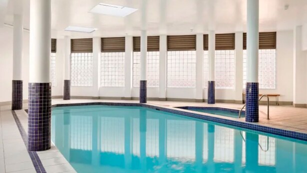 An indoor swimming pool with tiled walls, large windows with blinds, and a tiled floor. - Stunning Downtown Retreat With City Views (Surry Hills)