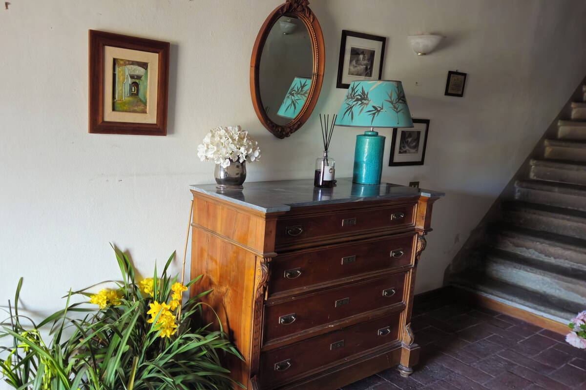 Een houten dressoir met lades, een spiegel, een vaas met bloemen en een lamp erbovenop.