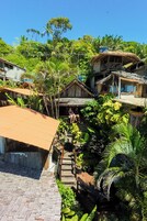 Uma vila rural com casas de madeira tradicionais, um caminho pavimentado e vegetação exuberante.