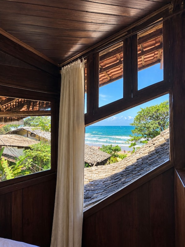 A room with a large window overlooking a beach and ocean. - Beach House NATUREZA (Itacare)