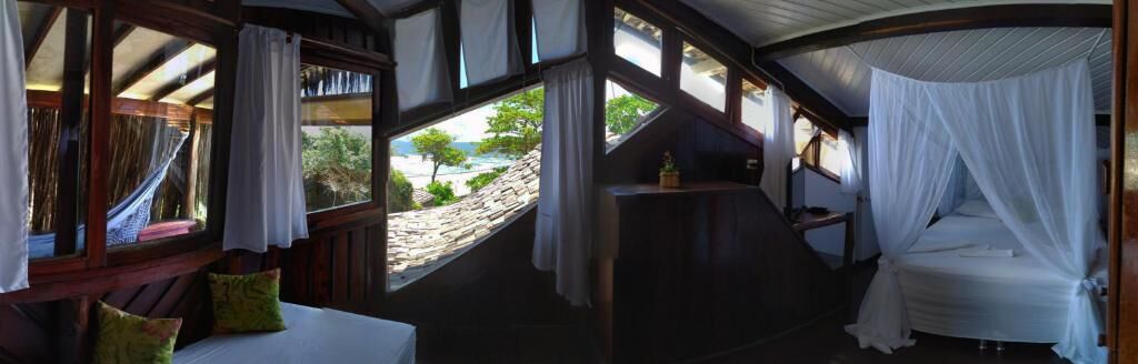 Un dormitorio con cama bajo dosel, ventanas amplias y vista a la playa.