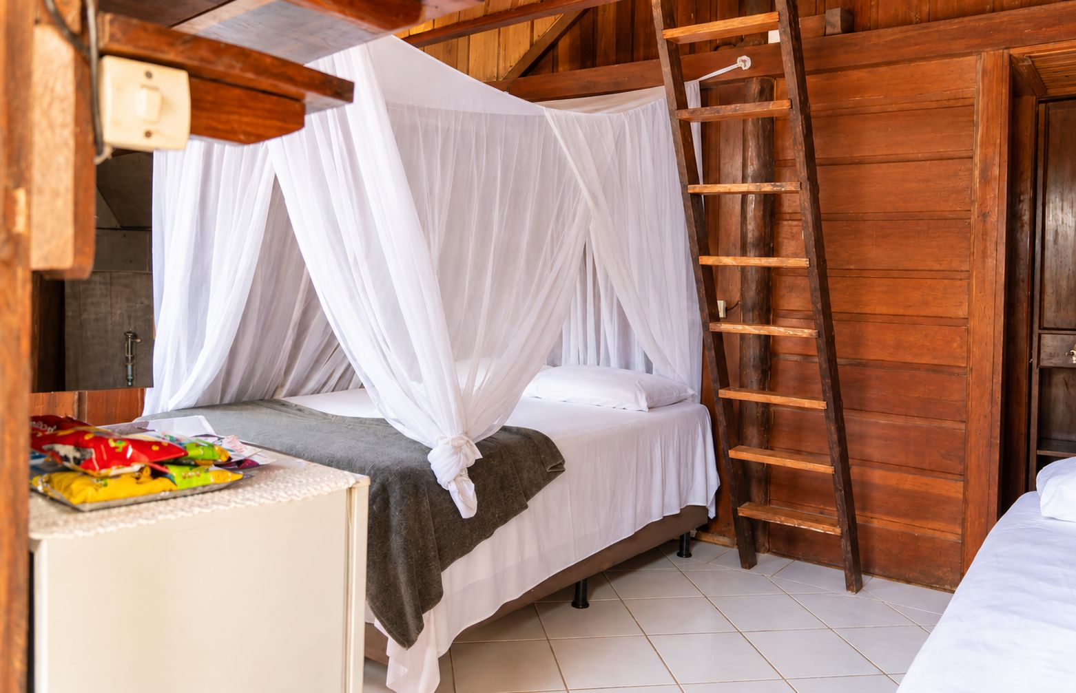Een kamer met een bed onder een hemelbed, een houten ladder en een betegelde vloer.