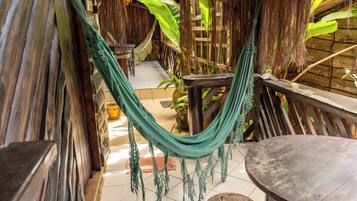 Una hamaca en una estructura de madera con suelo de baldosas, una mesa redonda y una planta en maceta.