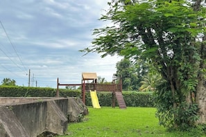 A concrete retaining wall, a wooden play structure with a slide, and a grassy area with trees.