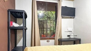Une chambre à coucher avec un lit, une fenêtre avec des rideaux, un téléviseur fixé au mur et une petite table.