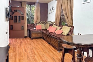 A cozy room with a wooden floor, a brown sofa with cushions, a small table, and a decorative wall piece.