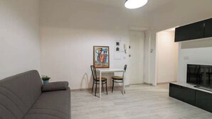 En moderne stue med sofa, spisebord med stole, fjernsyn og et billede på væggen.