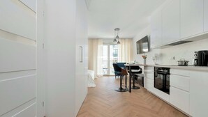 Eine moderne Küche mit weißen Schränken, ein Essbereich mit Tisch und Stühlen und ein Blick ins Freie.