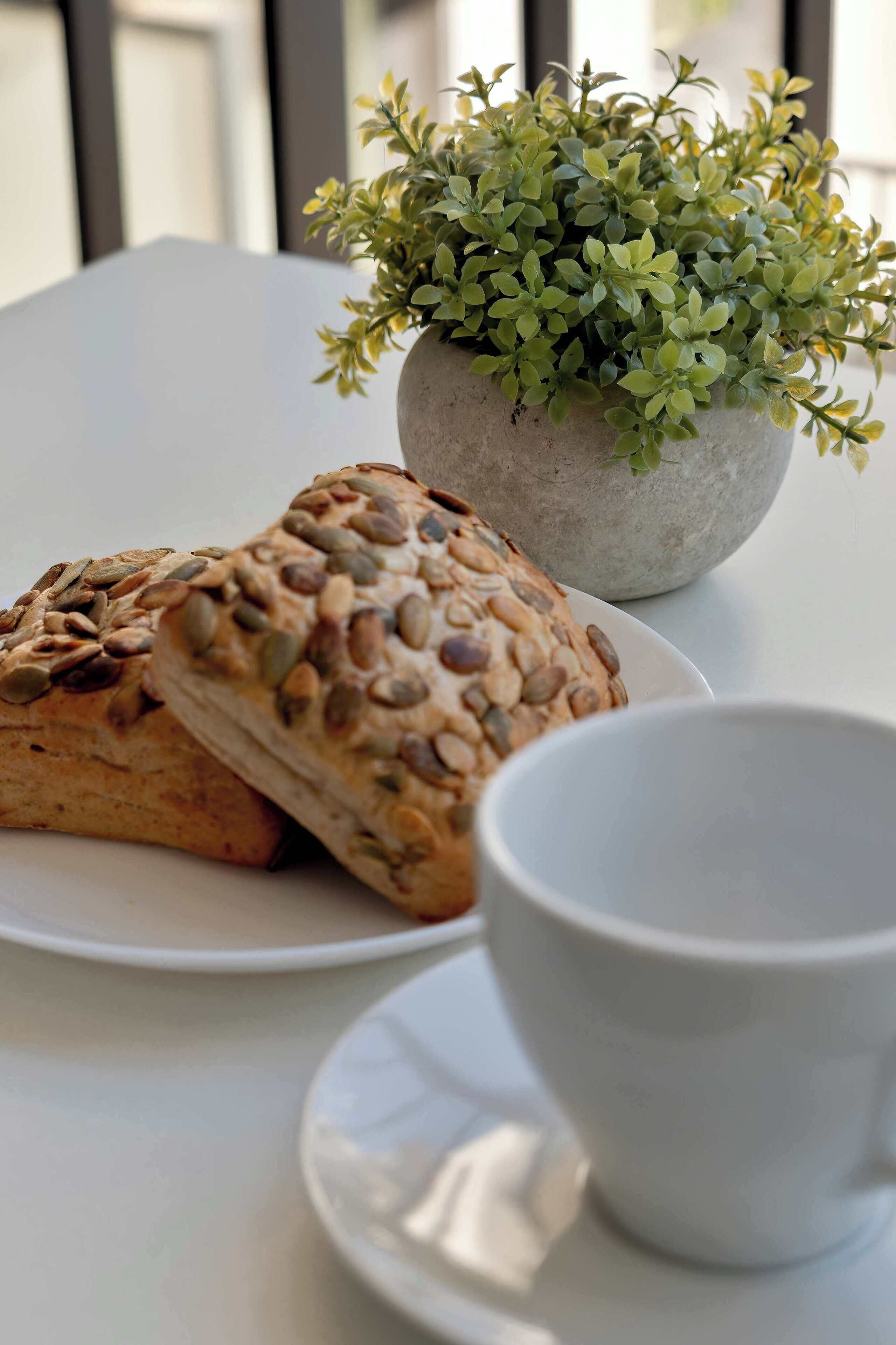 Uma mesa com um vaso de planta, dois pães e uma xícara.