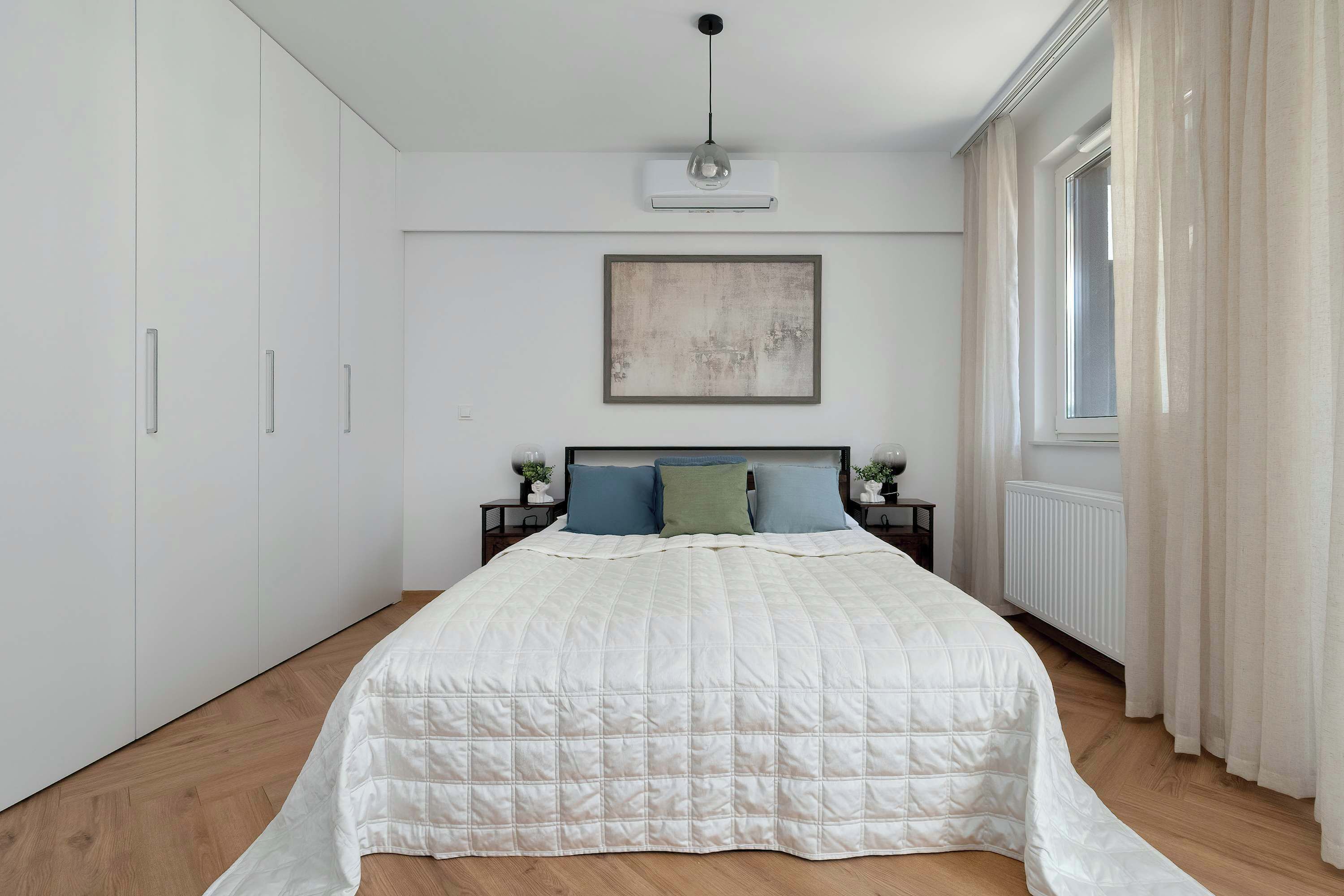 A bedroom with a large bed, a nightstand with a lamp, a ceiling fan, and a window with curtains.