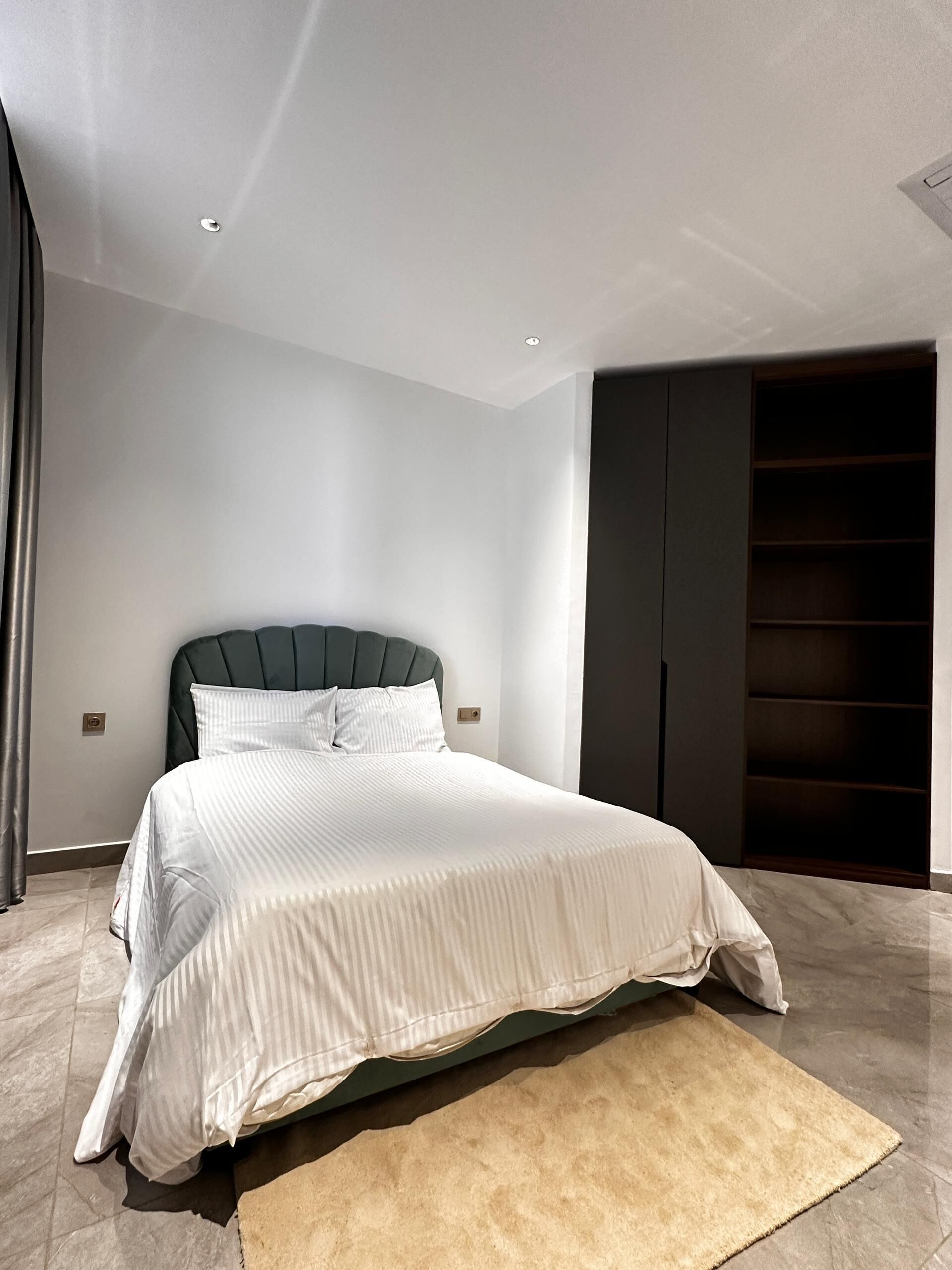 A modern bedroom with a large bed, a dark headboard, and a built-in wardrobe.