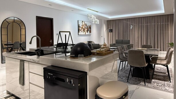 A modern kitchen with a built-in dishwasher, a dining area with a table and chairs, and a large island with a sink.