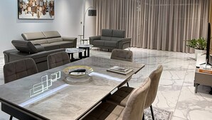 A modern living room with a dining area, featuring a marble table, leather sofas, and a contemporary light fixture.