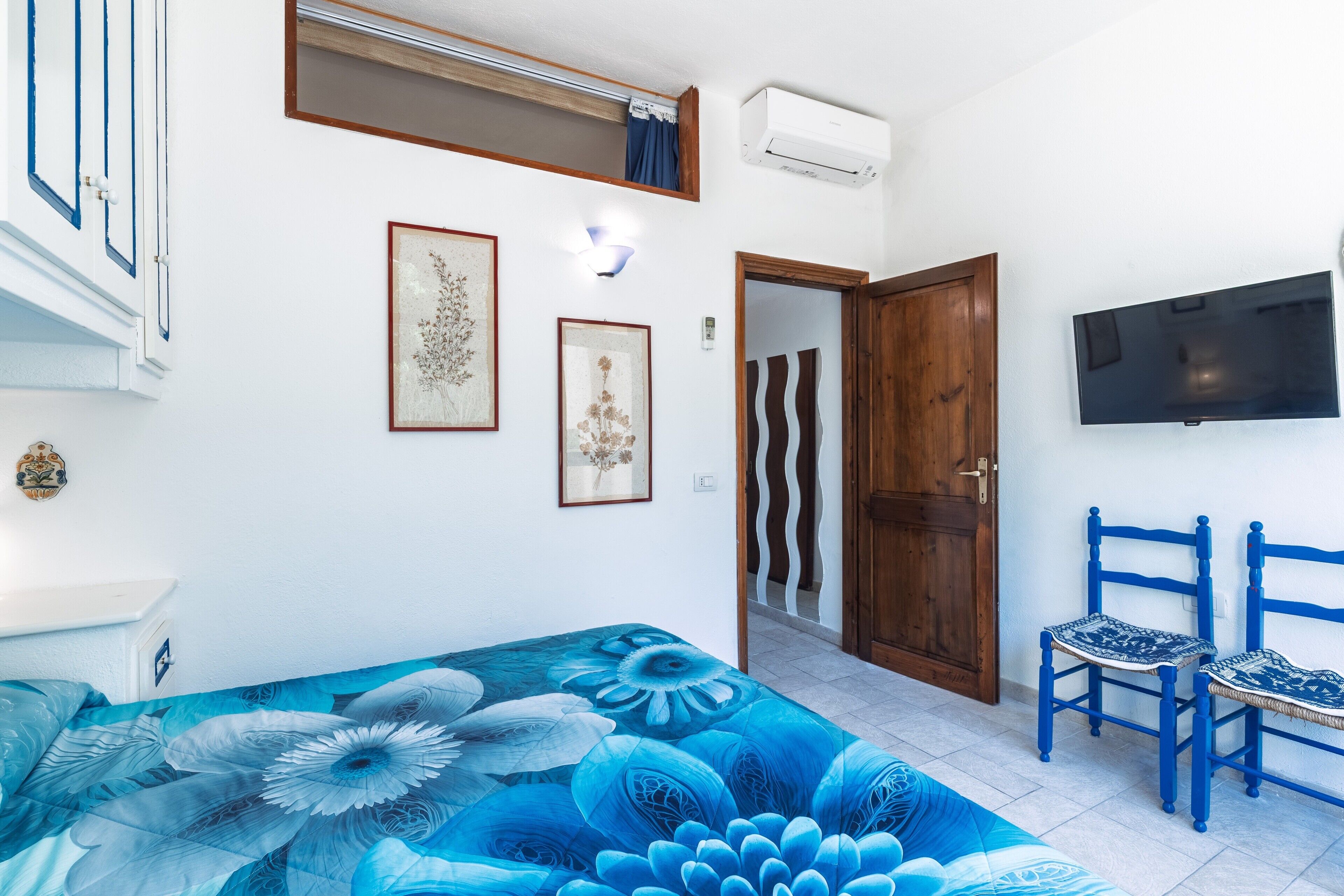 A bedroom with a bed, a TV, a door, and a window.