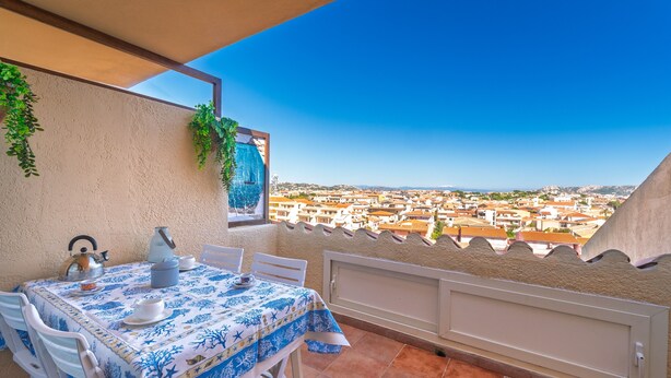 Ein Balkon mit Tisch für zwei Personen, Blick auf eine Stadtlandschaft und ein gerahmtes Bild an der Wand.