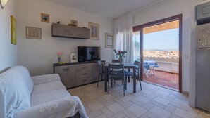 Ein Wohnzimmer mit einer Couch, einem Fernseher, einem Esstisch, Stühlen und einem Balkon mit Blick.