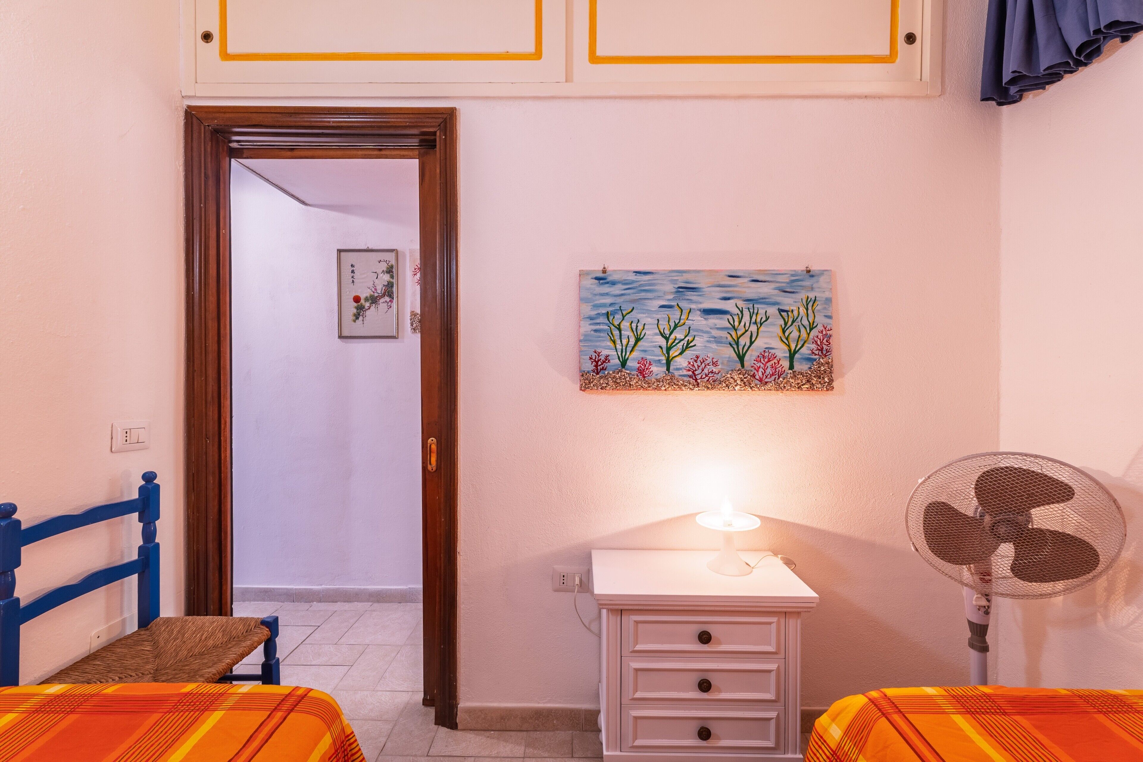 Une chambre à coucher avec un lit, une table de chevet, un ventilateur et un tableau accroché au mur.