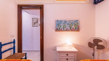 Une chambre à coucher avec un lit, une table de chevet, un ventilateur et un tableau accroché au mur.