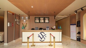 A hotel reception area with a marble floor, a reception desk with a logo, framed pictures on the wall, and a sign with instructions. - The Host Venu (Riyadh)