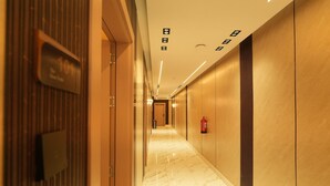 A hotel corridor with a marble floor, wooden paneling, and a fire extinguisher mounted on the wall. - The Host Venu (Riyadh)