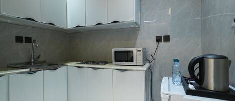 A modern kitchen with white cabinets, a microwave, a kettle, and a water bottle.