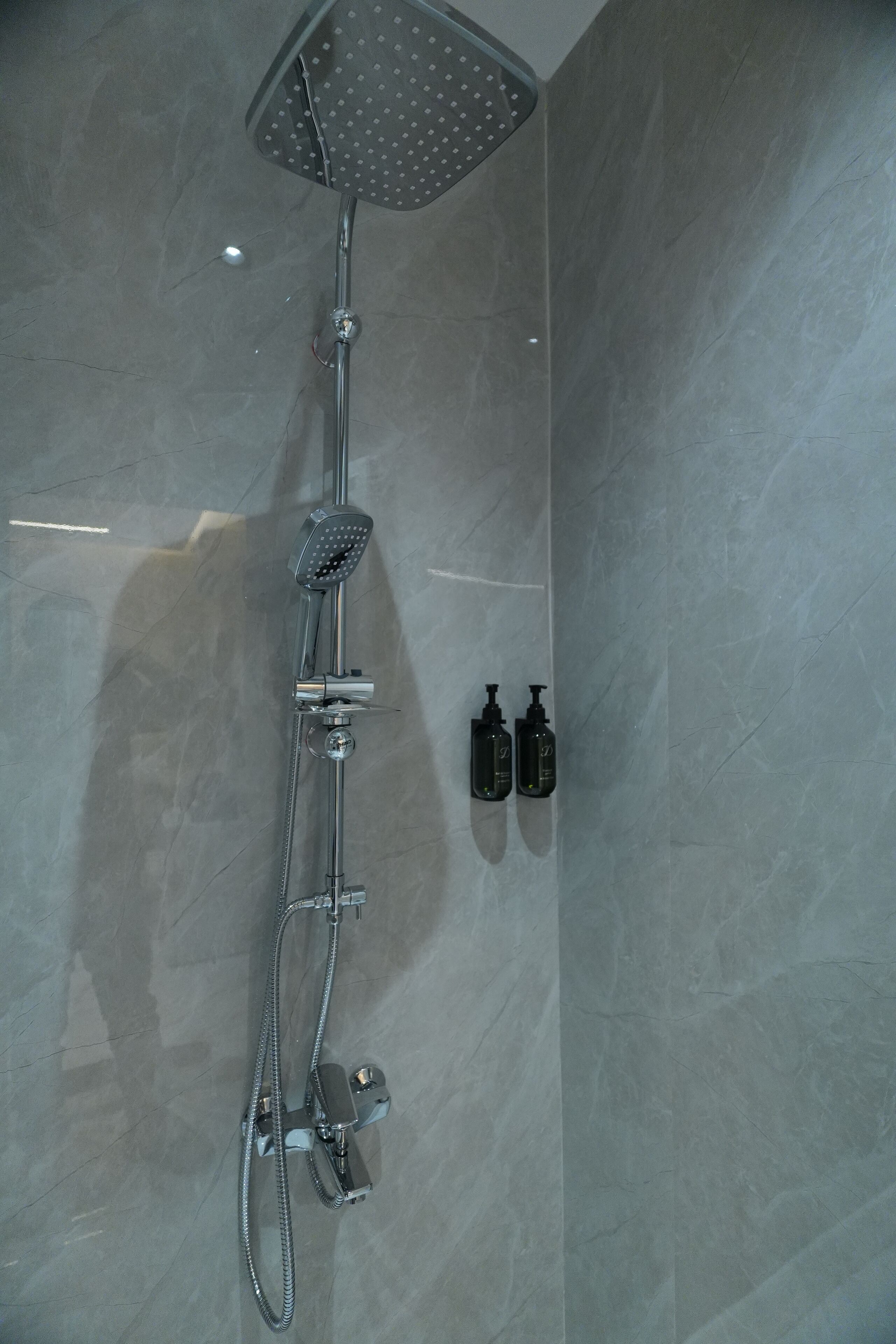 A modern shower with a handheld showerhead and a fixed rain showerhead, mounted on a wall with a sleek, tiled surface.