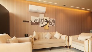 A modern living room with a beige sofa set, a wall-mounted air conditioner, and decorative calligraphy art. - The Host Venu (Riyadh)
