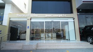A hotel entrance with a glass facade, a wheelchair accessibility sign, and a staircase leading up to the entrance. - The Host Venu (Riyadh)