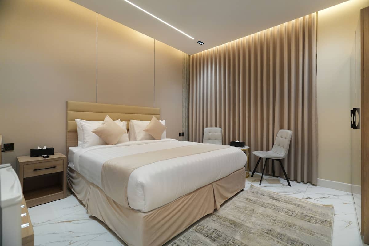 A modern bedroom with a large bed, bedside tables, a chair, and a large window with curtains.