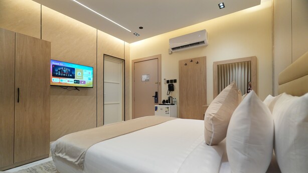 A modern hotel room with a large bed, a flat-screen TV mounted on the wall, a minibar, and a built-in air conditioning unit. - The Host Venu (Riyadh)