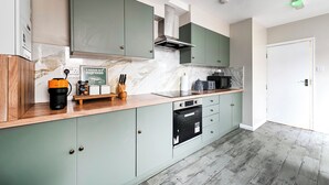 A modern kitchen with green cabinets, a marble countertop, and a built-in oven. -  Modern Watford Hub | 4 bedroom/sleeps 8 | 25 Mins to London + 5 Mins to Center (Watford)