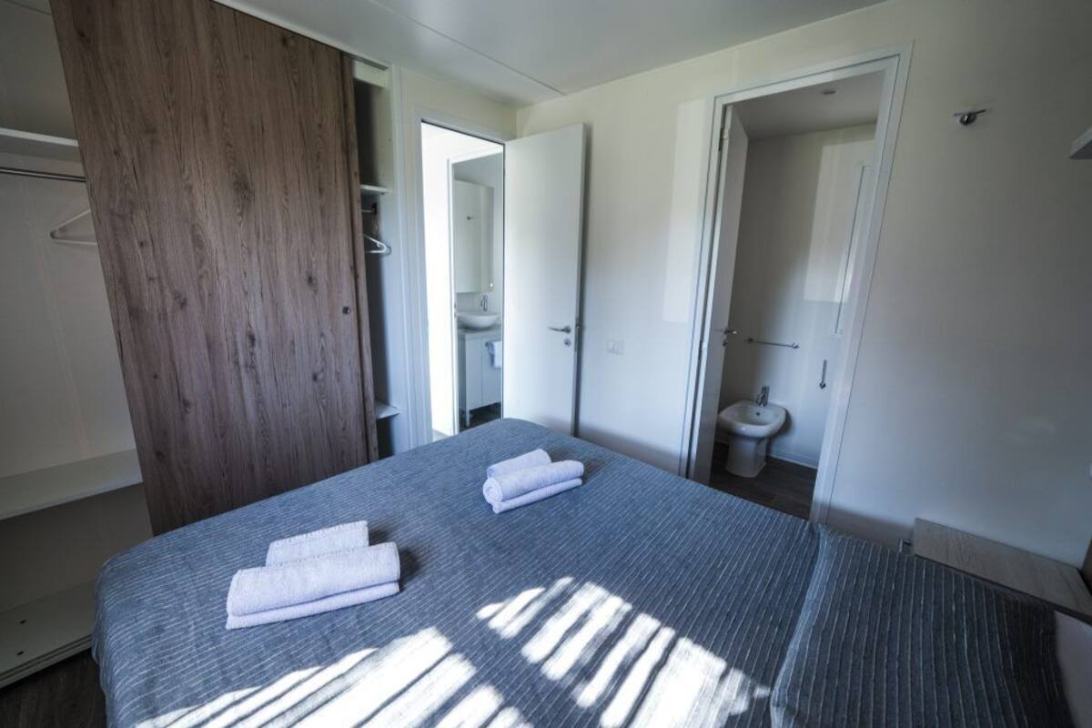 A modern hotel room with a bed, a wooden wardrobe, a bathroom with a bidet, and a shower.