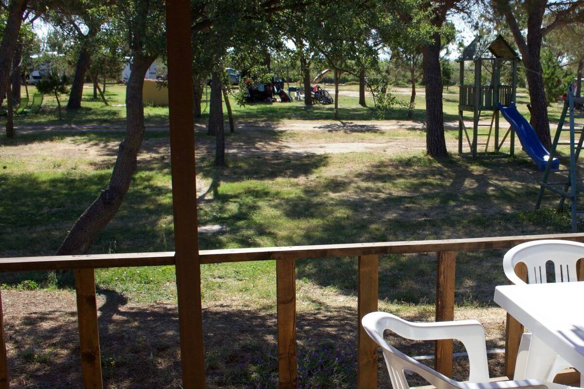 A covered outdoor area with a table and chairs, surrounded by trees and a playground.