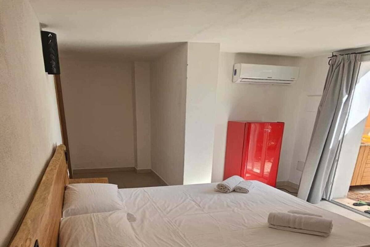A single bed with white linens, a wooden headboard, a small round wooden table, and a red cabinet.