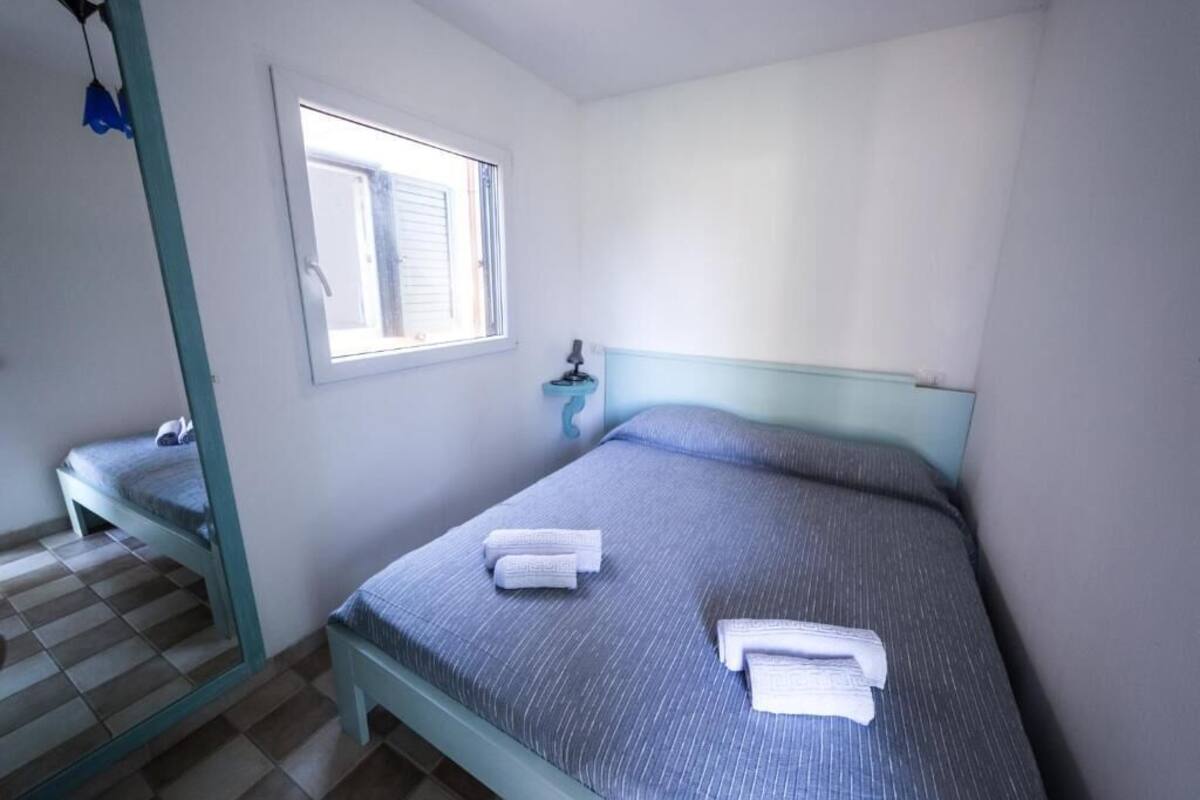 A bedroom with a bed, a window, a bedside table, and a mirror.
