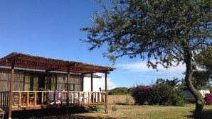 Una baita di legno con veranda, immersa in un prato e circondata da alberi.