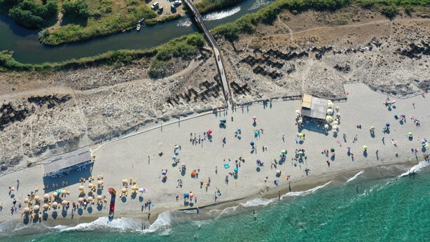 Vista aerea di una spiaggia con persone, ombrelloni e un molo.