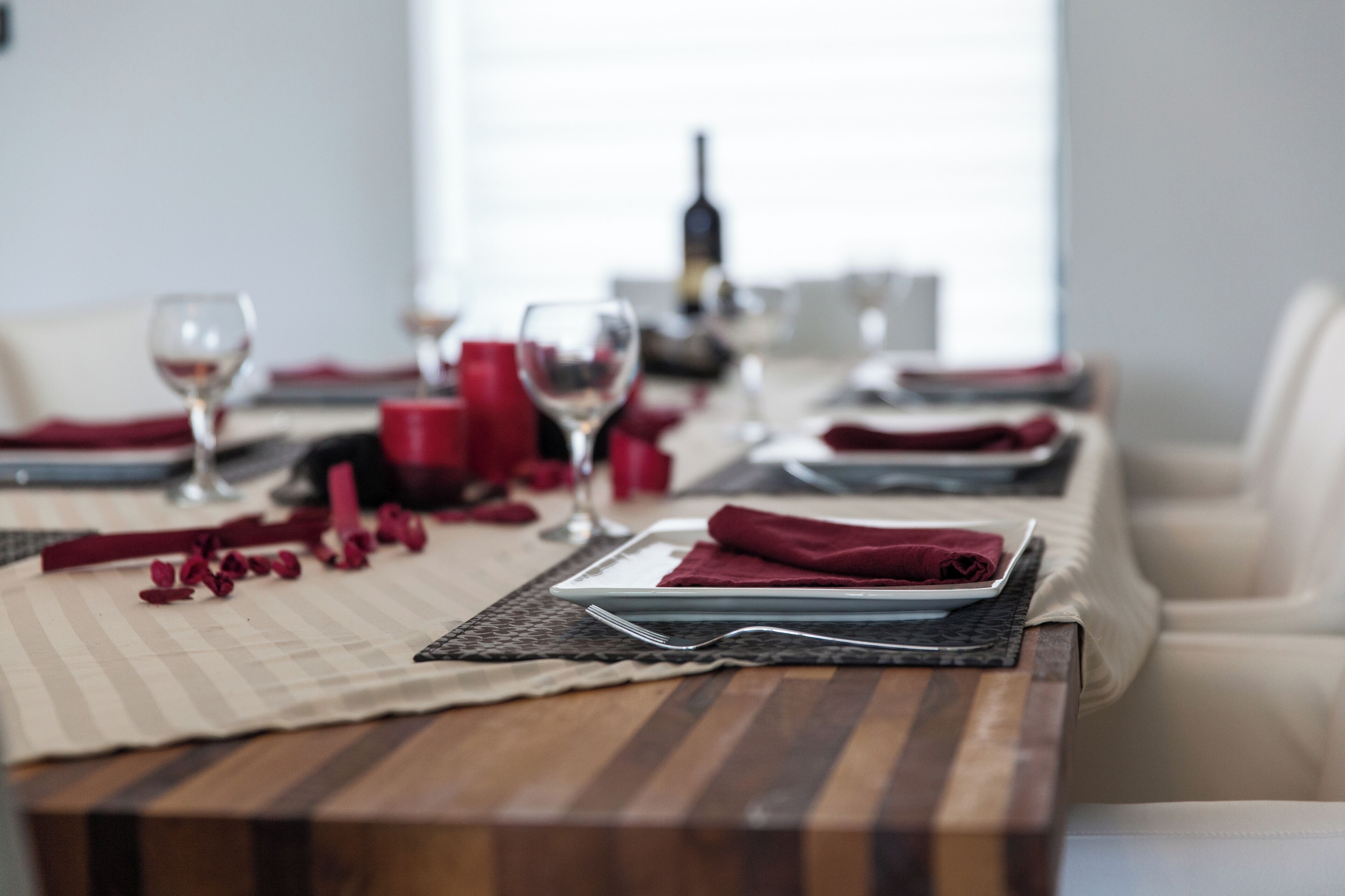 A dining table set with red napkins, wine glasses, and a bottle in the background.