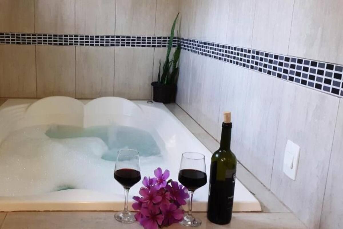 A bathtub with a bottle of wine and two glasses of red wine.