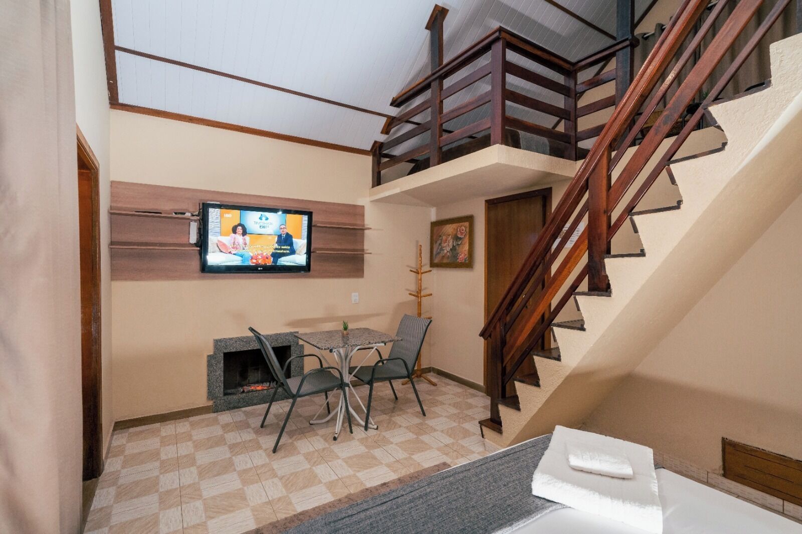 A hotel room with a TV, a fireplace, a dining area, and a staircase.