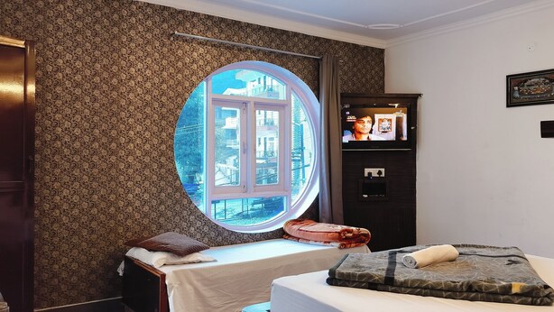 Ein Schlafzimmer mit rundem Fenster, einem Bett mit gemustertem Überwurf, einem Nachttisch, einem Kleiderschrank und einem an der Wand befestigten Fernseher.